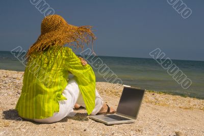 Woman sitting on beach with laptop