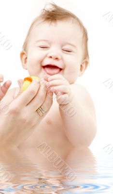 laughing baby boy in water playing with rubber duck
