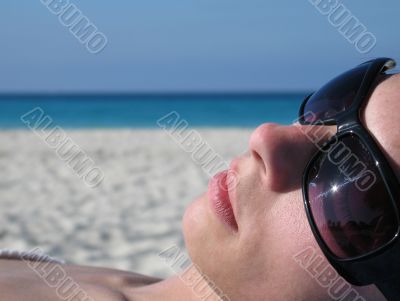 girl with sunglasses tanning on the beach