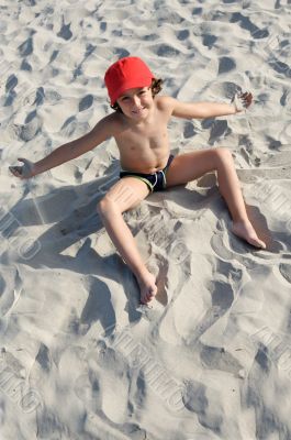 Pretty boy sitting on the sand from the beach