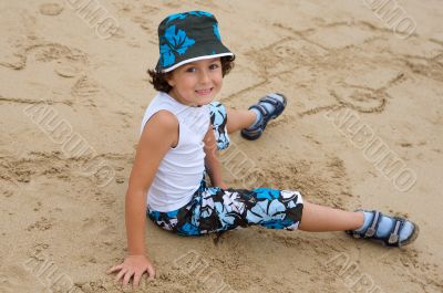 Pretty boy sitting on the sand from the beach