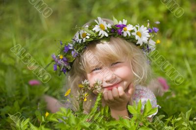 happy little girl in flowers wreath lying on green grass