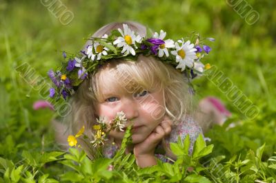 happy little girl in flowers wreath lying on green grass