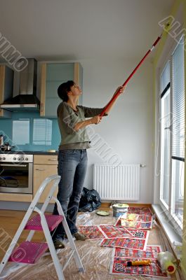 Young woman paints a wall in the kitchen