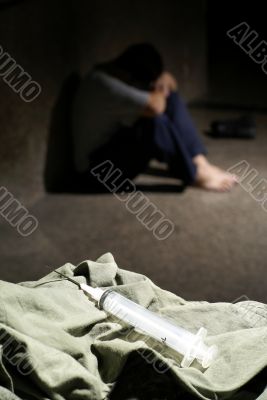 Syringe and drud addict in dark background