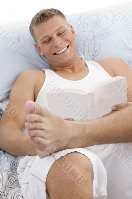 smiling handsome male reading book in bed