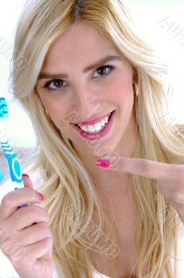 front view of smiling woman pointing at toothbrush