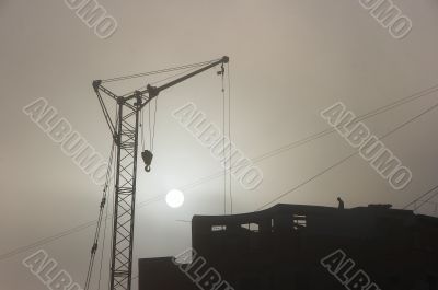 Gray sunset sky with lifting construction cranes
