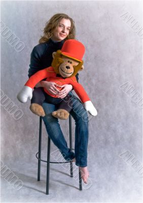 Beautiful girl is holding a toy monkey in hands.