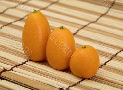 Three fresh kumquat against a mat