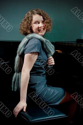 young girl sitting near piano in dress smiling