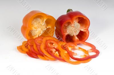 Cut orange and red sweet pepper showing seeds with slices on whi