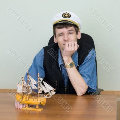 Man in a uniform cap at table with ship