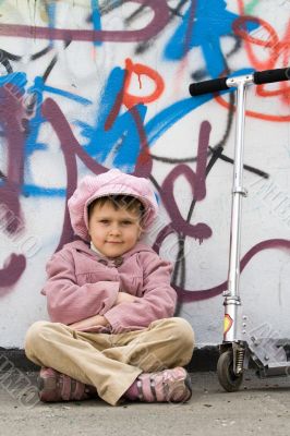 Funny little girl with scooter near graffiti wall