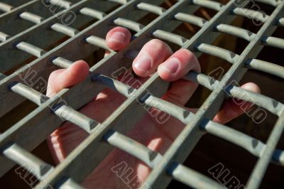 Man`s hand protrudes from a cage holding on