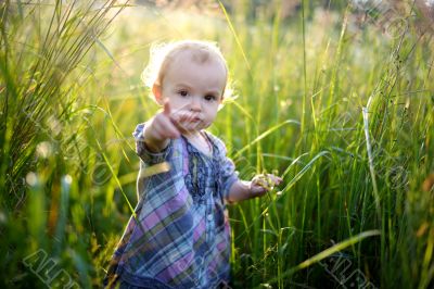 Little baby in an overgrown grass pointing at you