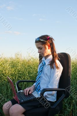 Teen girl sitting with a laptop at field