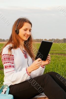 Young lady with e-book reader sitting on grass