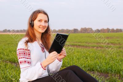 Young lady with e-book reader sitting on grass