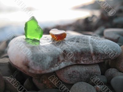 Green and orange glass laying on the sea shore
