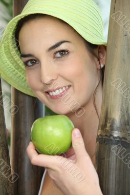Woman stood by wooden poles holding a green apple