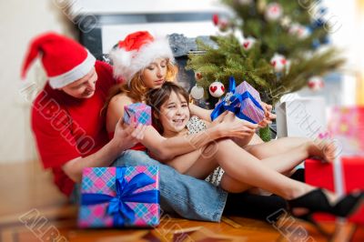 Young happy family near a Christmas tree at home holding gifts.