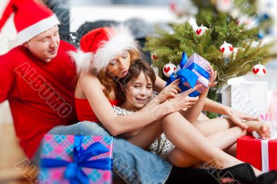 Young happy familye near a Christmas tree at home holding gifts.