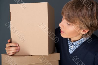 Portrait of young man holding on box against grey wall.