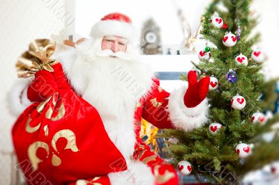Santa sitting at the Christmas tree, near fireplace and looking.