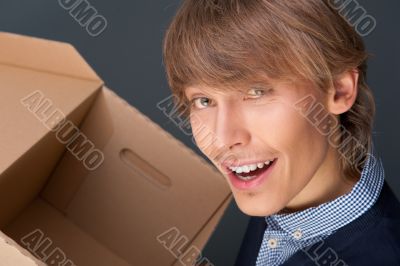 Portrait of young man holding on box against grey wall. 