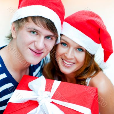 Young happy couple in Christmas hats standing together and holdi