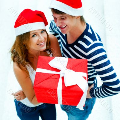 Young happy couple in Christmas hats standing together and holdi
