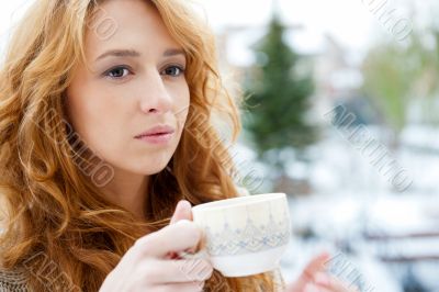 Portrait of beautiful red hair girl drinking coffee on winter ba