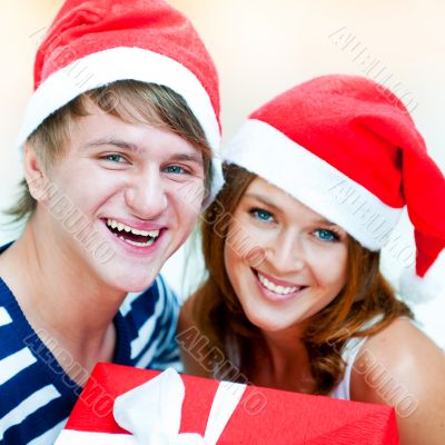 Young happy couple in Christmas hats standing together and holdi