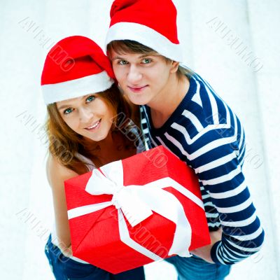 Young happy couple in Christmas hats standing together and holdi
