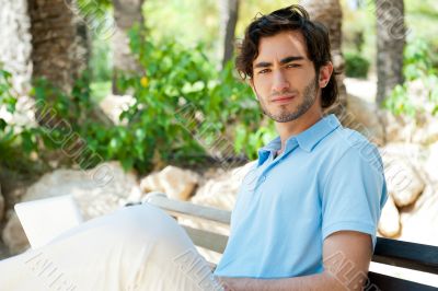 Portrait of a young man with laptop outdoor sitting on bench