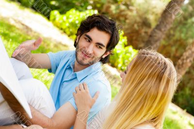 Happy couple of students with a notebook sitting on grass at cam