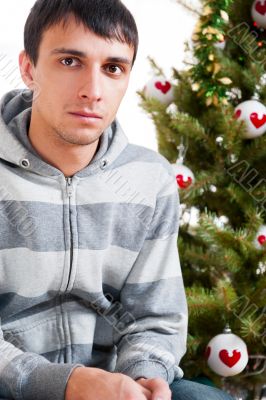 Young calm man sitting in front of Christmas tree