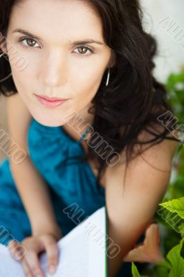 Beautiful girl sitting at park and reads the book. Looking up at