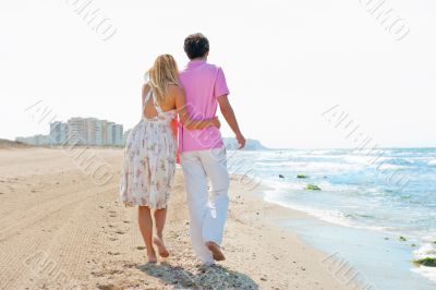 Couple at the beach holding hands and walking. Sunny day, bright