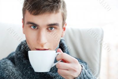 Portrait of a young man drinking coffee while sitting on armchai