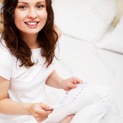 Happy woman reading a letter in her bedroom. She recieved a lett