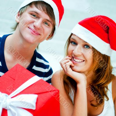 Young happy couple in Christmas hats standing together and holdi
