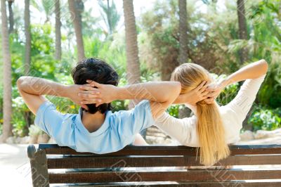 Smiling beautiful couple sitting on a banch at summer park and d