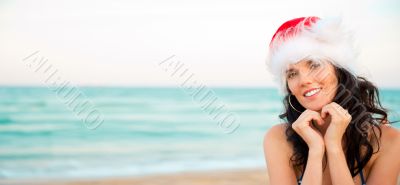 Young beautiful woman wearing christmas hat showing heart shape 