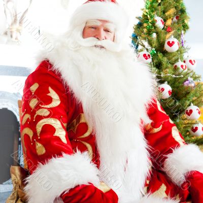Santa sitting at the Christmas tree, fireplace and looking at ca
