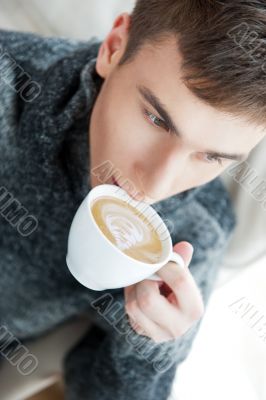 Portrait of a young man drinking coffee while sitting on armchai