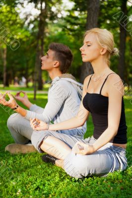 Portrait of young beautiful couple sitting in lotus pose on gree