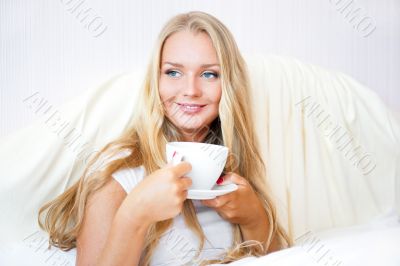 Smiling woman drinking a coffee lying on a bed at home or hotel.