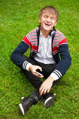 Student outside sitting on green grass and listening music via h